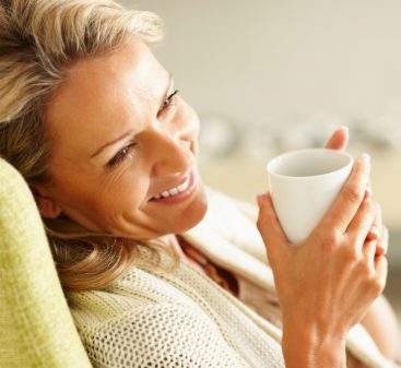 Woman smiling resting back in a chair holding a mug of tea